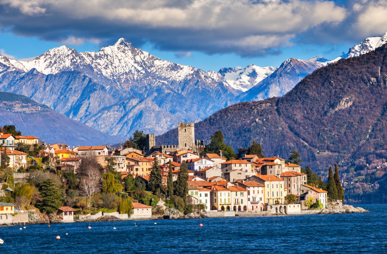 Lakeside village with a castle and snow-capped mountains in the background